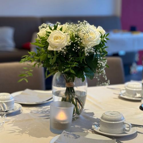 Gedeckter Tisch mit weißen Rosen in der Vase